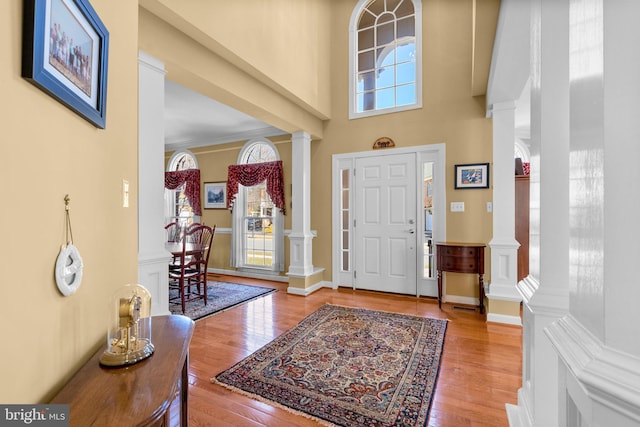 foyer with crown molding, hardwood / wood-style flooring, ornate columns, and a towering ceiling