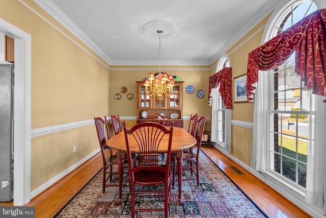 dining space with hardwood / wood-style flooring, crown molding, and an inviting chandelier