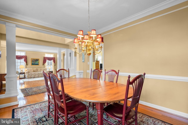 dining area featuring decorative columns, hardwood / wood-style floors, crown molding, and an inviting chandelier