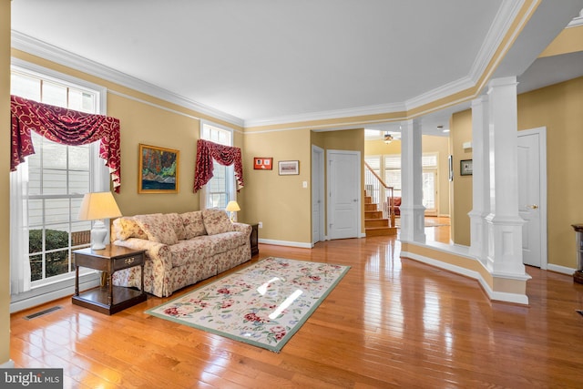 living room featuring decorative columns, ornamental molding, and light wood-type flooring