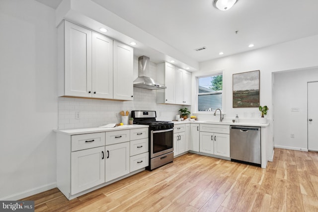 kitchen featuring tasteful backsplash, white cabinets, light hardwood / wood-style floors, stainless steel appliances, and wall chimney range hood