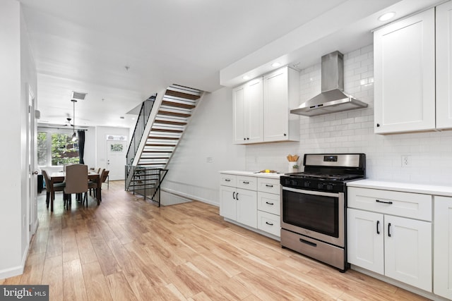 kitchen featuring wall chimney range hood, decorative backsplash, gas stove, and white cabinets