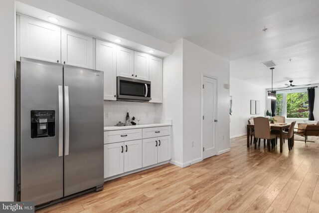 kitchen with pendant lighting, appliances with stainless steel finishes, white cabinetry, tasteful backsplash, and light hardwood / wood-style floors