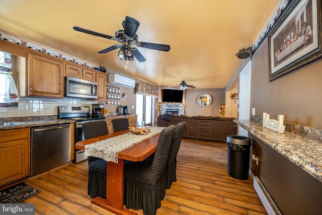 kitchen with hardwood / wood-style floors, a stone fireplace, a wall unit AC, appliances with stainless steel finishes, and backsplash