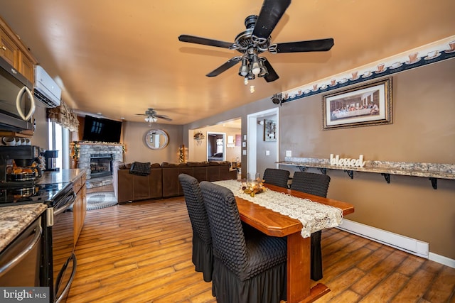 dining room featuring light wood-type flooring, ceiling fan, and a fireplace