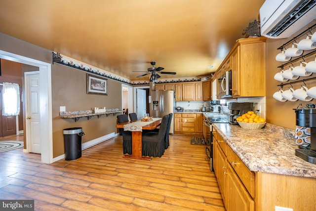 kitchen with appliances with stainless steel finishes, light hardwood / wood-style floors, ceiling fan, light stone counters, and a wall mounted air conditioner