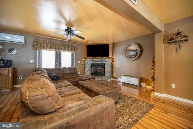 living room featuring ceiling fan, light hardwood / wood-style flooring, a stone fireplace, and a wall unit AC