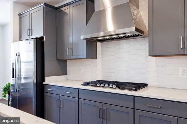 kitchen featuring wall chimney exhaust hood, tasteful backsplash, light stone countertops, and appliances with stainless steel finishes