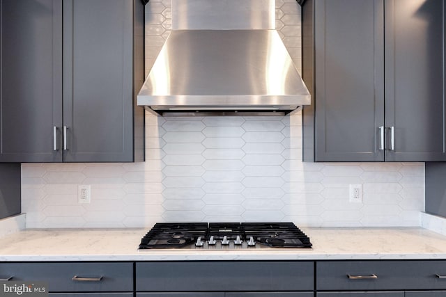 kitchen with wall chimney exhaust hood, gray cabinetry, tasteful backsplash, light stone counters, and stainless steel gas stovetop