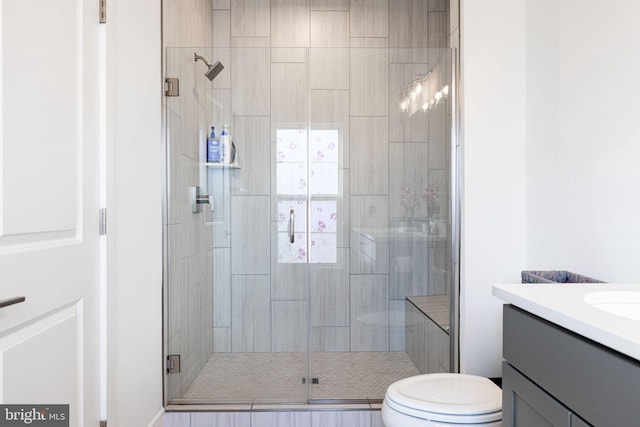 bathroom featuring a shower with shower door, toilet, and vanity