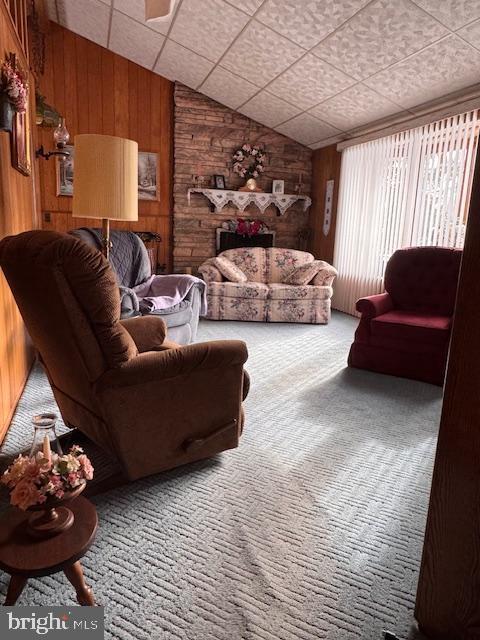 carpeted living room with vaulted ceiling and wood walls