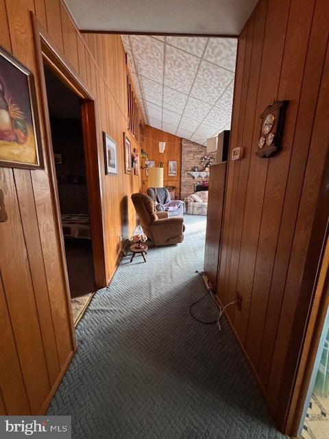 hallway with lofted ceiling, carpet floors, and wood walls