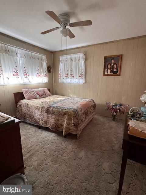 carpeted bedroom featuring ceiling fan and wood walls