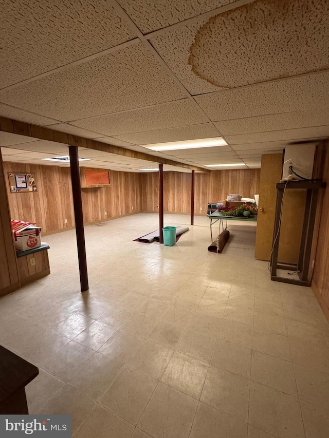 basement with a paneled ceiling and wood walls