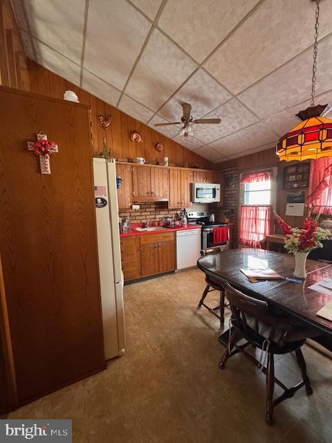 kitchen with vaulted ceiling, stainless steel appliances, ceiling fan, and wood walls