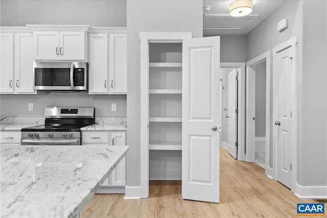 kitchen with appliances with stainless steel finishes, light hardwood / wood-style flooring, white cabinetry, and light stone countertops