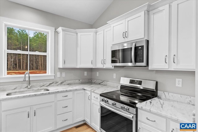 kitchen featuring light stone countertops, appliances with stainless steel finishes, white cabinetry, sink, and vaulted ceiling