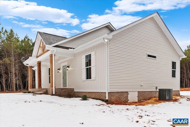 view of snowy exterior with central AC unit and a porch