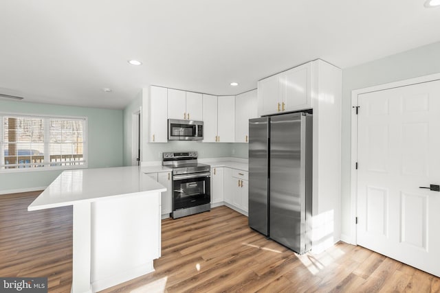 kitchen with stainless steel appliances, white cabinets, light hardwood / wood-style floors, and kitchen peninsula