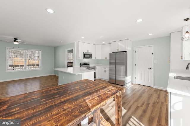 kitchen with appliances with stainless steel finishes, wood-type flooring, white cabinets, a kitchen island, and decorative light fixtures