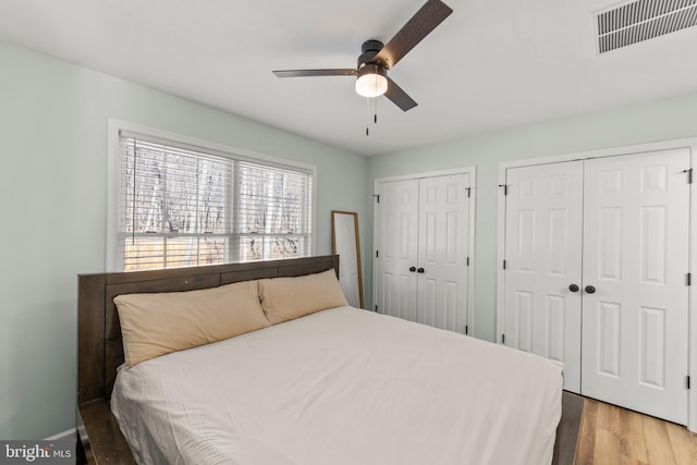 bedroom with hardwood / wood-style flooring, ceiling fan, and two closets