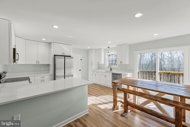 kitchen with white cabinetry, sink, kitchen peninsula, stainless steel appliances, and light wood-type flooring