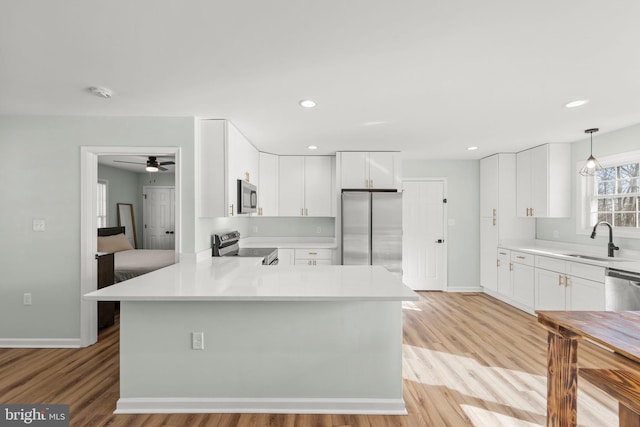 kitchen featuring sink, white cabinetry, hanging light fixtures, light wood-type flooring, and stainless steel appliances