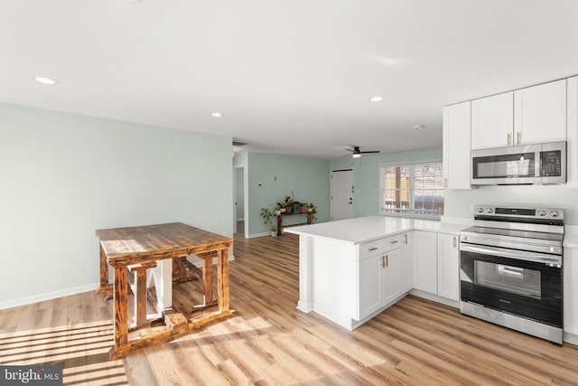 kitchen with appliances with stainless steel finishes, white cabinets, ceiling fan, kitchen peninsula, and light wood-type flooring