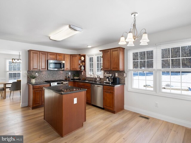 kitchen with a notable chandelier, a kitchen island, sink, hanging light fixtures, and stainless steel appliances