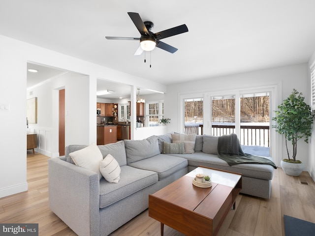 living room featuring ceiling fan with notable chandelier and light hardwood / wood-style flooring