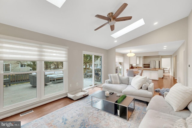 living room featuring ceiling fan, high vaulted ceiling, light wood-type flooring, and a skylight