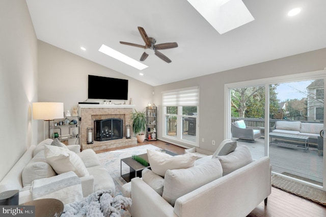 living room featuring high vaulted ceiling, a skylight, wood-type flooring, ceiling fan, and a brick fireplace