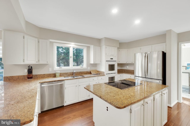 kitchen featuring appliances with stainless steel finishes, sink, white cabinets, a center island, and light stone counters