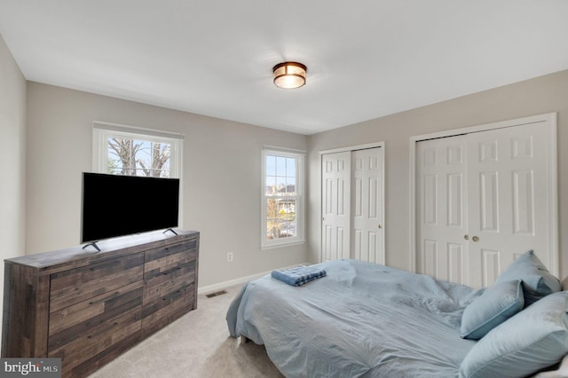 bedroom featuring light carpet, multiple windows, and multiple closets