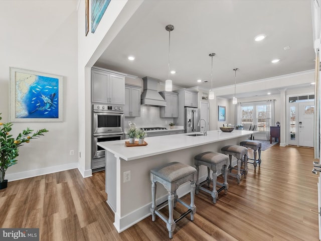 kitchen with decorative light fixtures, stainless steel appliances, premium range hood, a breakfast bar, and gray cabinetry