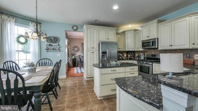 kitchen with stainless steel appliances, tasteful backsplash, dark stone countertops, pendant lighting, and cream cabinets