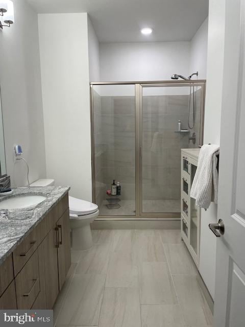 bathroom featuring toilet, a shower with shower door, and vanity