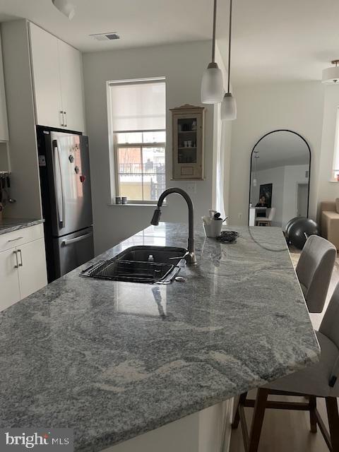 kitchen featuring a breakfast bar area, white cabinets, hanging light fixtures, and stainless steel refrigerator