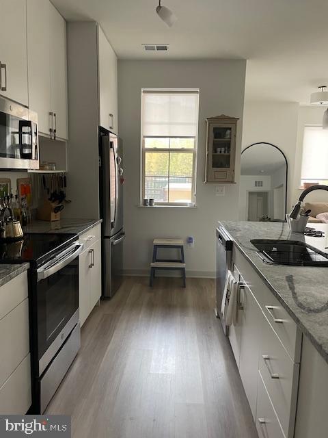 kitchen with light stone countertops, appliances with stainless steel finishes, white cabinetry, wood-type flooring, and sink