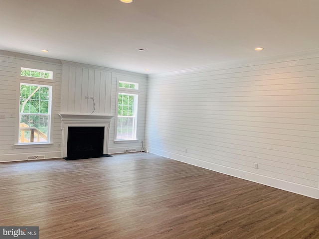 unfurnished living room with dark wood-type flooring, a wealth of natural light, and wood walls