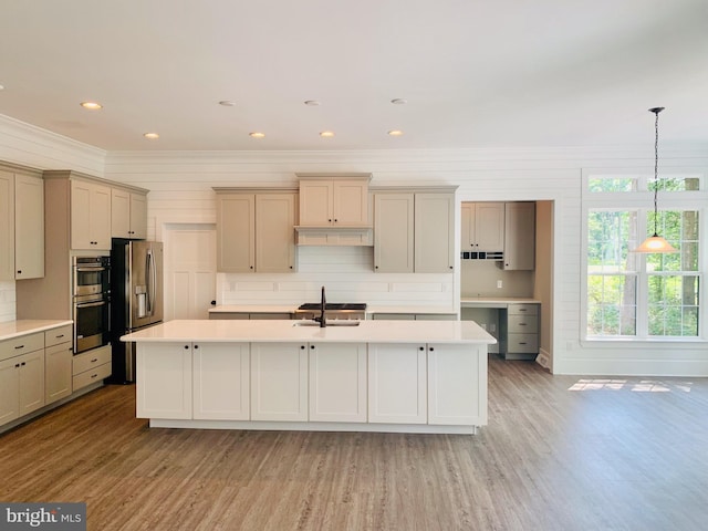 kitchen featuring appliances with stainless steel finishes, backsplash, a kitchen island with sink, hanging light fixtures, and sink