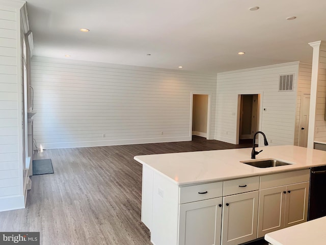 kitchen with sink, black dishwasher, wooden walls, and an island with sink