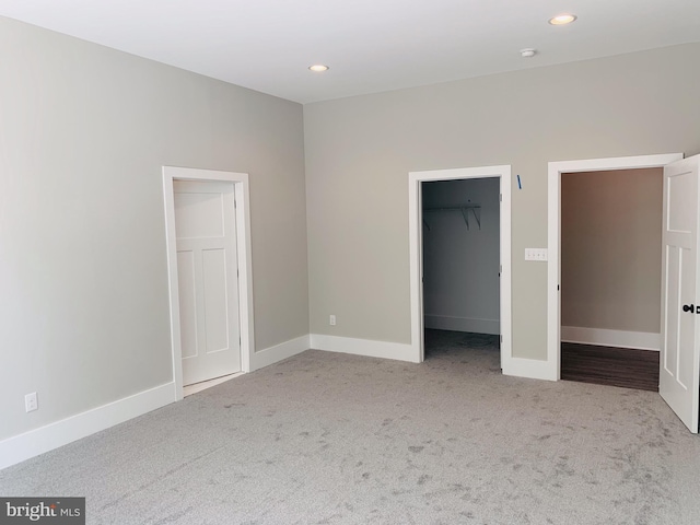 unfurnished bedroom with a walk in closet, a closet, and light colored carpet