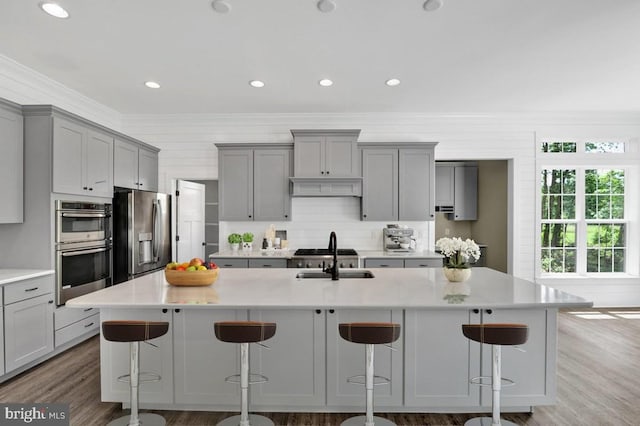 kitchen with stainless steel appliances, a kitchen breakfast bar, backsplash, a kitchen island with sink, and gray cabinetry