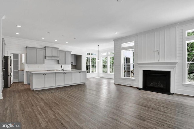 kitchen featuring dark wood-type flooring, a large fireplace, stainless steel fridge, and an island with sink