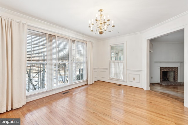 unfurnished dining area featuring ornamental molding, a chandelier, hardwood / wood-style floors, and a fireplace