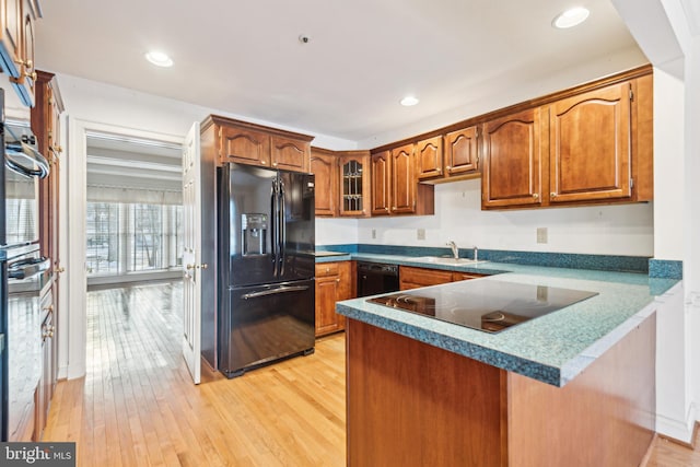 kitchen with sink, black appliances, light hardwood / wood-style flooring, and kitchen peninsula