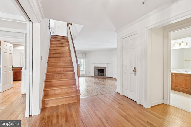 stairway featuring a brick fireplace, hardwood / wood-style floors, and ornamental molding