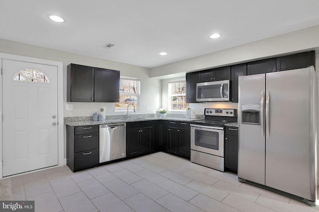 kitchen with recessed lighting, stainless steel appliances, dark cabinetry, and light stone countertops