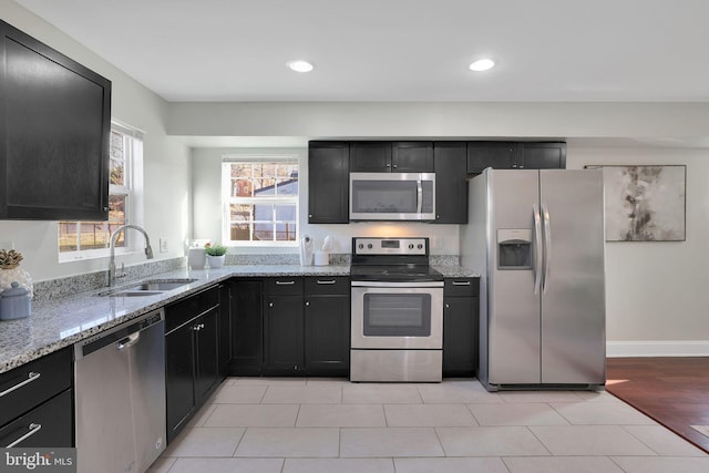 kitchen featuring a sink, stainless steel appliances, light stone counters, and dark cabinetry